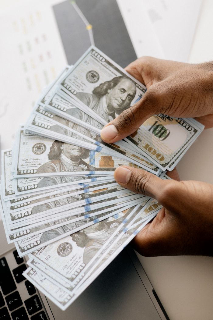 Crafting Captivating Headlines: Your awesome post title goes here Close-up view of hands counting U.S. hundred dollar bills over a laptop background.